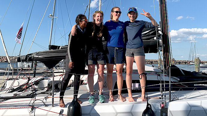 Group of female sailors stand posing for group photograph on their racing sailboats deck
