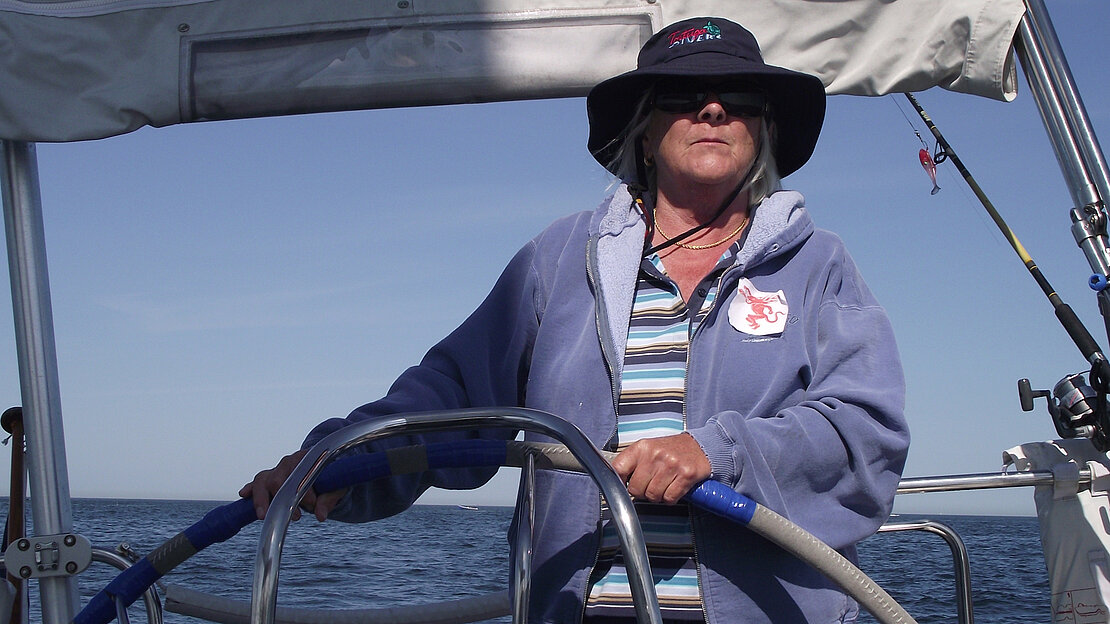 A stylish woman in a hat and sunglasses is steering the Dehler yacht Jester on a beautiful day out at sea.