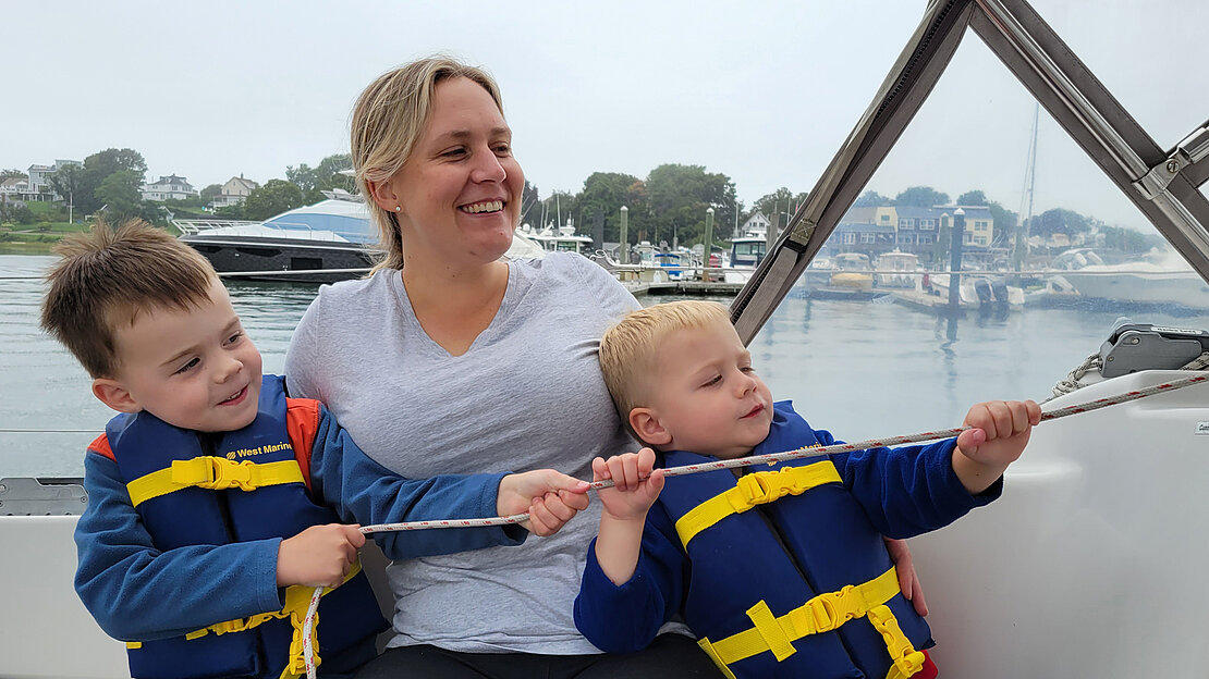 En el yate Dehler Jester, una mujer y sus dos hijos navegan juntos, sujetando una cuerda, valorando su tiempo en familia en el mar.