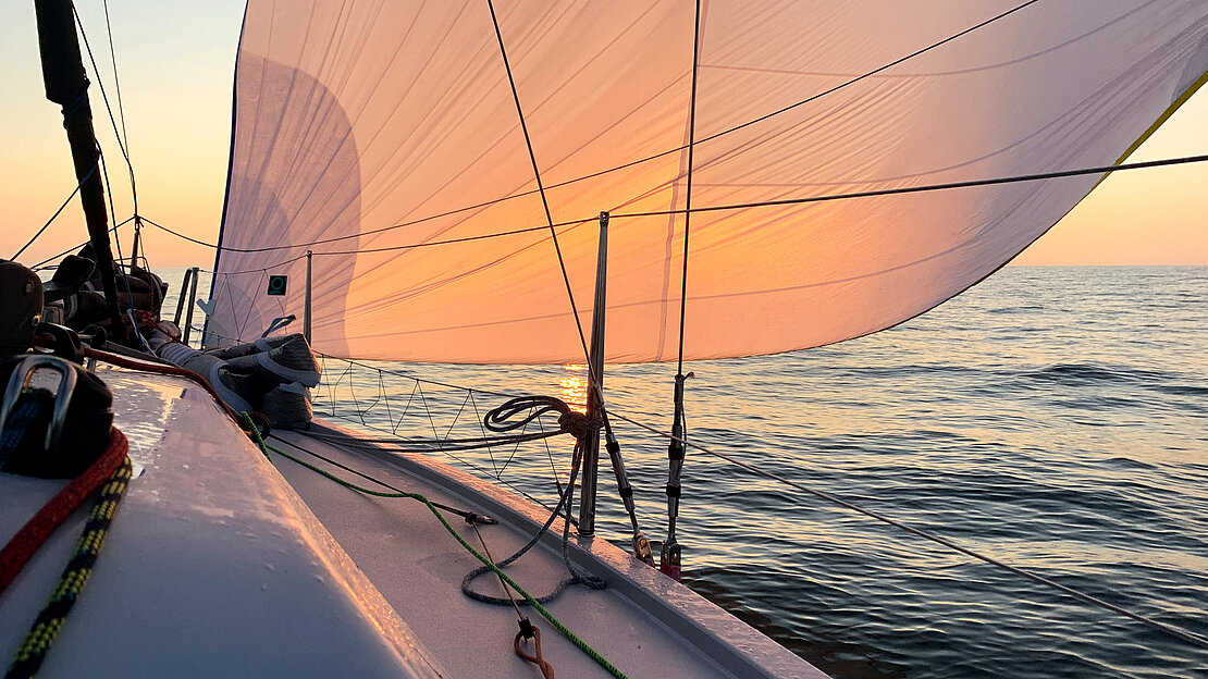 Racing sailboat sail under wind at sunset
