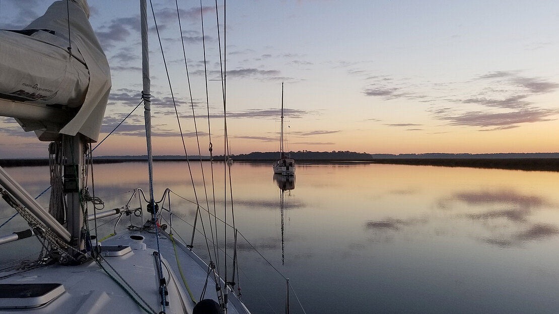 宁静的日落景象: Dehler游艇Jester宁静地停泊在平静的河流上，其帆船的剪影被美丽地照亮。