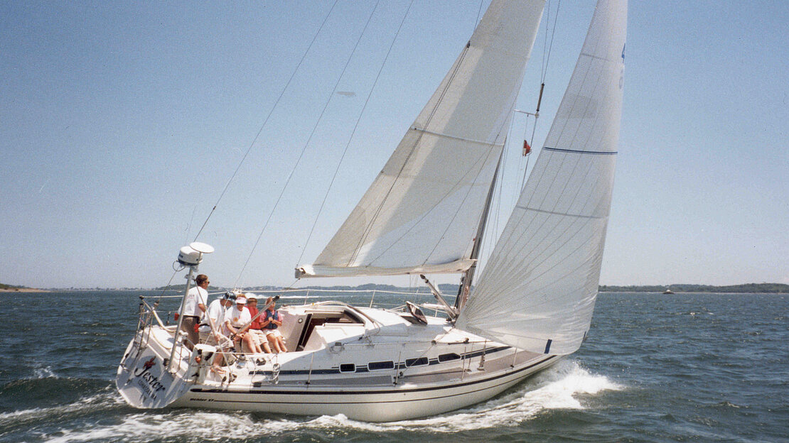 Un magnifique yacht Dehler nommé Jester glisse élégamment sur l'eau, orné d'une famille joyeuse profitant d'une aventure luxueuse en voilier.