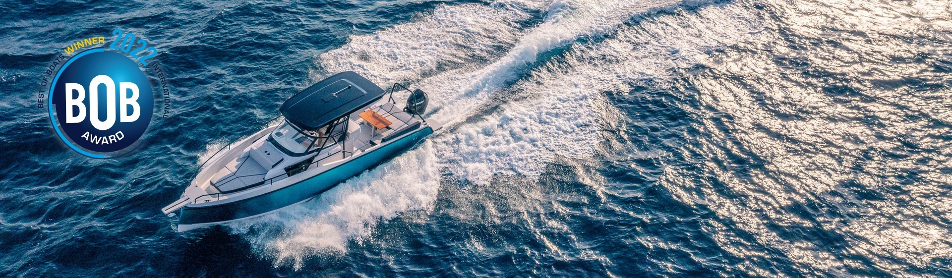 Un yacht Ryck 280 bleu à moteur unique, avec un grand pont pour prendre le soleil à l'avant et une table à manger à l'arrière, traverse l'océan à toute vitesse.