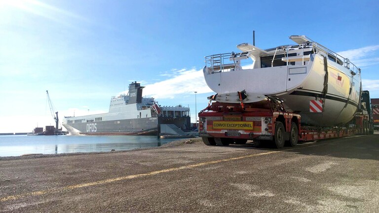 Sailing yacht is transferred to cargo ship on lowboy trailer