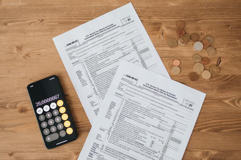 A calculator and financial documents sit on a wooden table.