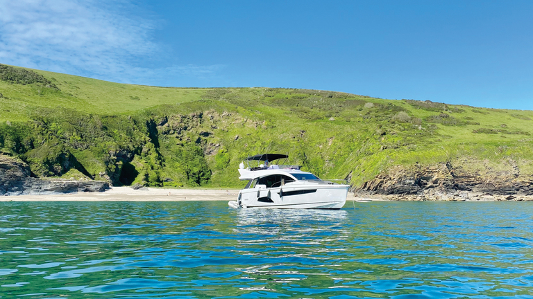 Sealine F530 yacht sull'acqua al litorale esotico, erba verde, cielo blu chiaro, acqua blu tropicale.