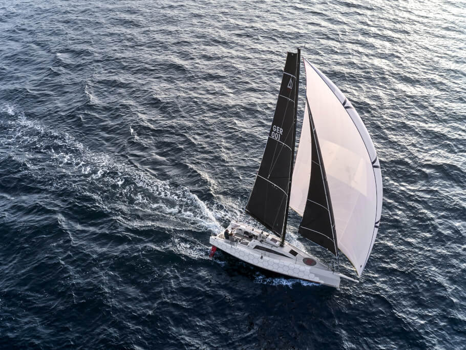 Aerial view of a white yacht with dark and white sails