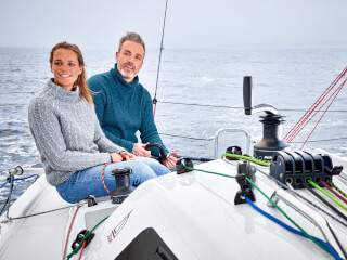 a man and a woman sitting in the cockpit of a yacht