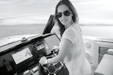 Jeune femme avec lunettes de soleil à la barre du yacht à moteur FJORD 44 open