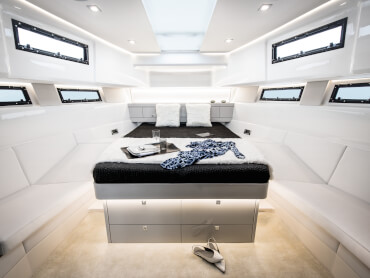 Fjord 48 open Interior view owner´s cabin | Island double berth with indirect lighting, painted furniture, pale acacia flooring, sofa, opening hatches, opening coachroof portholes, opening portlights | Fjord