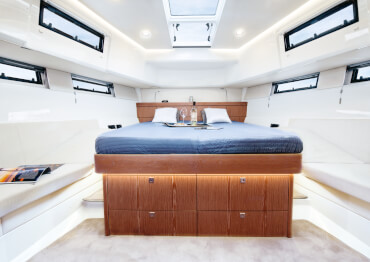 Fjord 48 open Interior view owner´s cabin | Island double berth with indirect lighting and drawers, mahogany wood style furniture, pale acacia flooring, sofa, opening hatches, opening coachroof portholes, opening portlights | Fjord